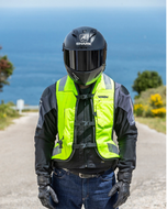 Motorcyclist on a coastal road wearing the high-vis Turtle 2 airbag vest over a riding jacket