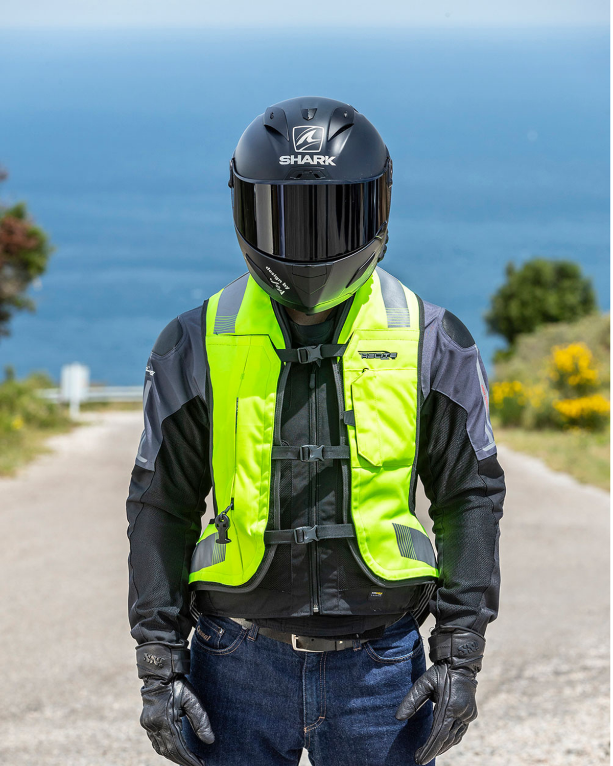 Motorcyclist on a coastal road wearing the high-vis Turtle 2 airbag vest over a riding jacket