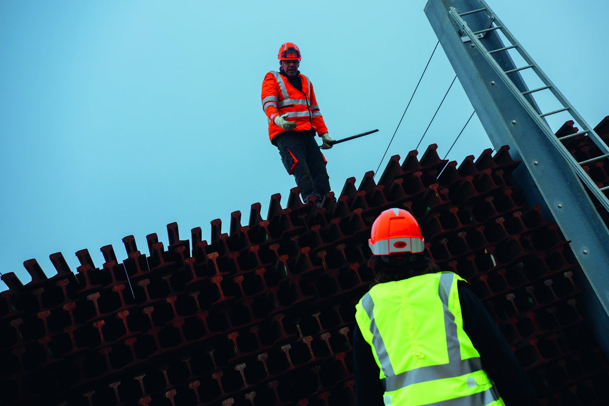 A worker standing on a stack of steel rails at height, talking to a colleague below