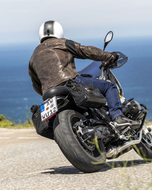 Rider seen from behind on a coastal road wearing the brown Roadster leather jacket