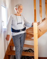 Older woman holding a stair rail at home while wearing the Helite Hip'Guard airbag belt