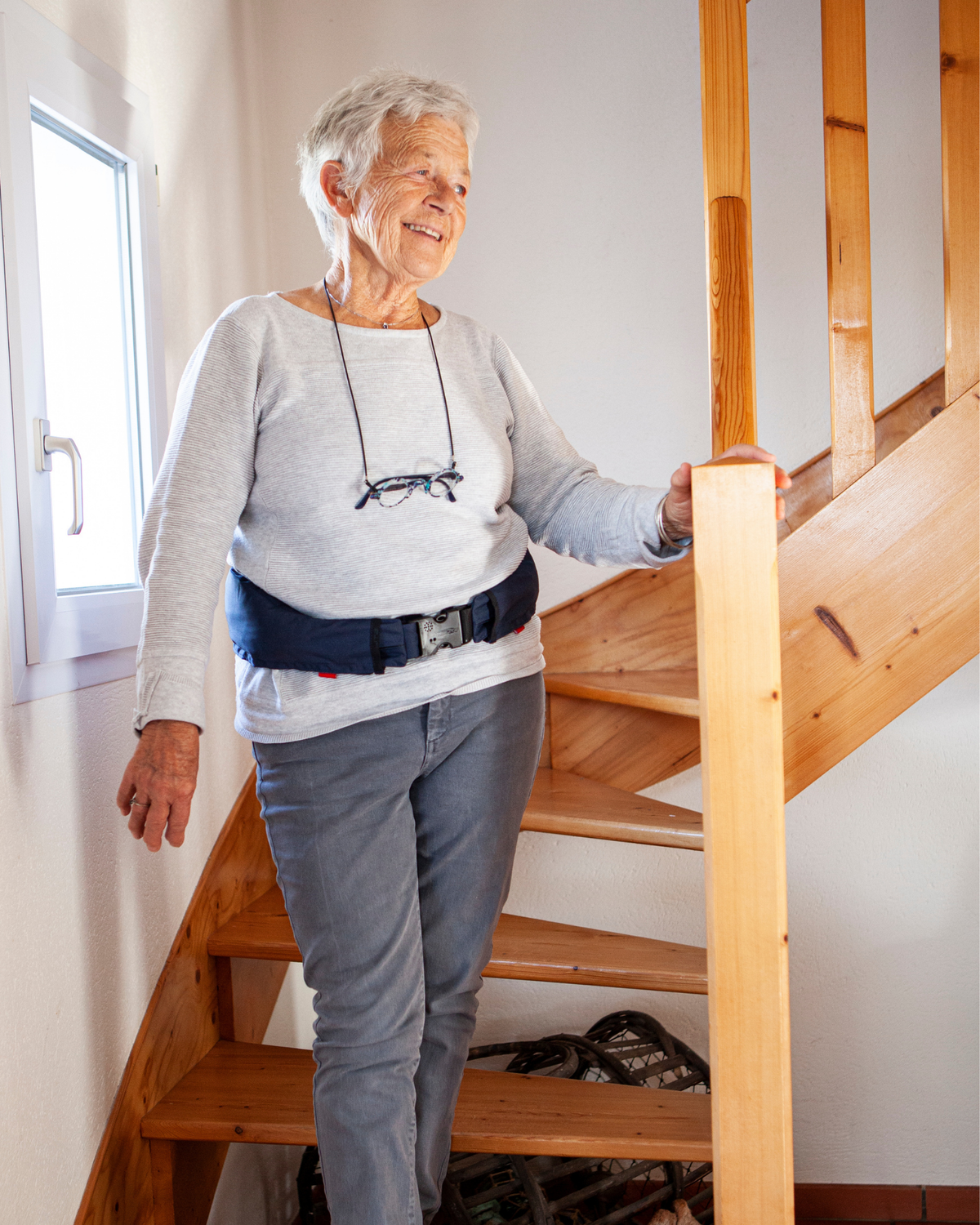 Older woman holding a stair rail at home while wearing the Helite Hip'Guard airbag belt